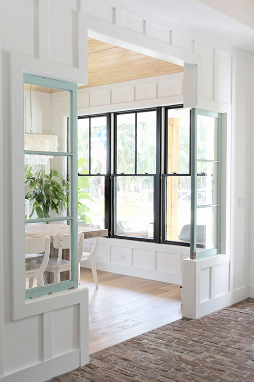 farmhouse dining room, entryway, brick floor, antique windows, architectural salvage, chandelier, west elm, wood floor, black windows, white walls, money tree, board and batten