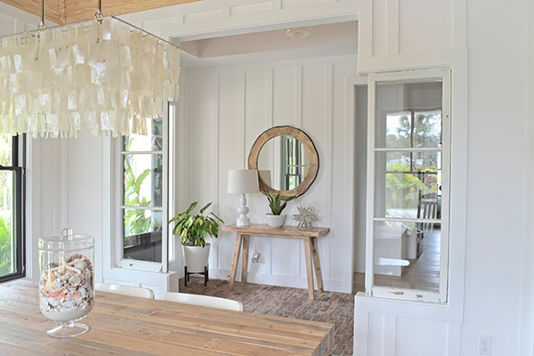 farmhouse dining room, entryway, capiz chandelier, west elm, table, white lamp, round wood mirror, seashells, beach cottage, white walls, board and batten
