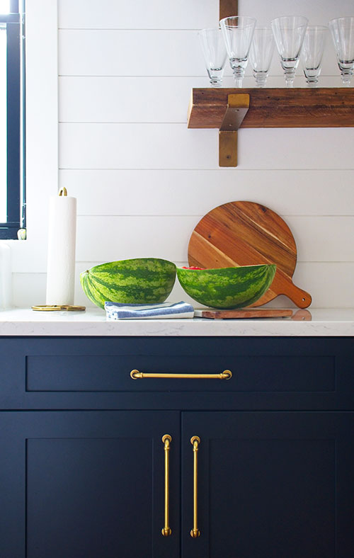 farmhouse kitchen navy blue cabinets brass hardware open shelving watermelon cutting board paper towel holder