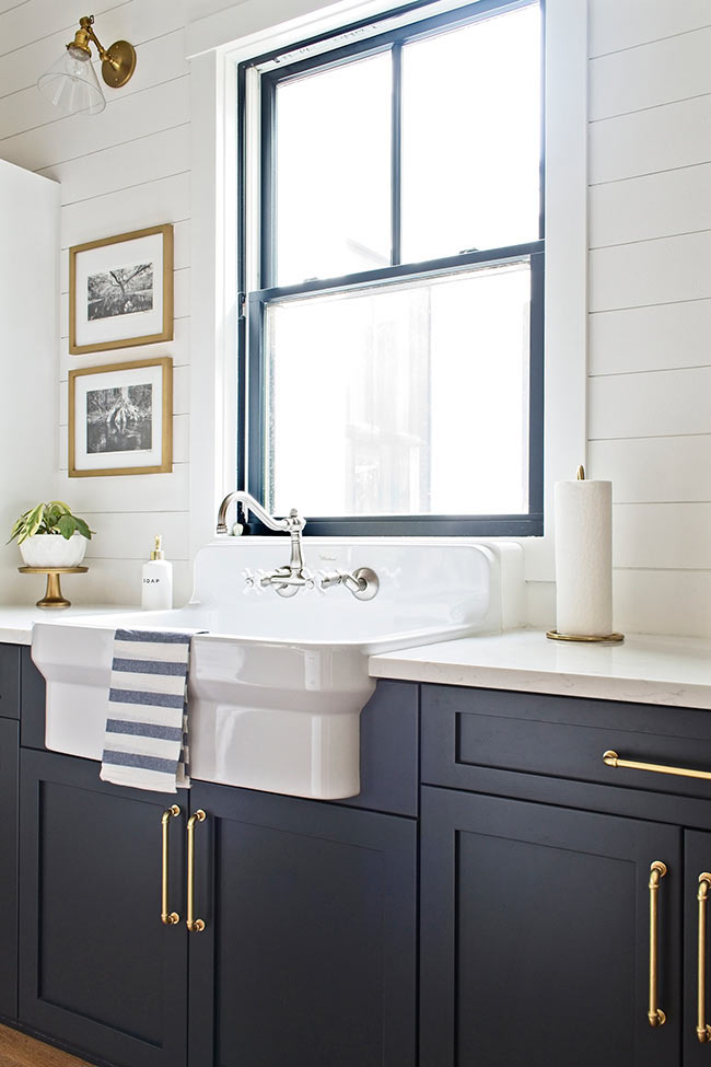 modern farmhouse cottage kitchen with navy blue cabinets with satin brass hardware and apron farmhouse sink in front of window