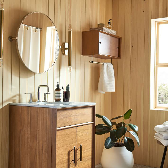 round brass pivot mirror on wood panel bathroom wall above vanity