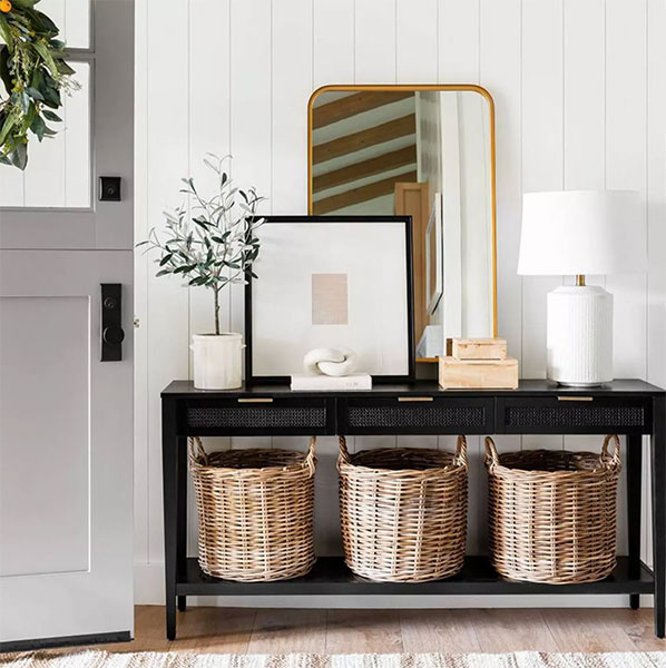brass gold rectangular mirror leaning against wall on top of black console table with lamp and 3 rattan baskets