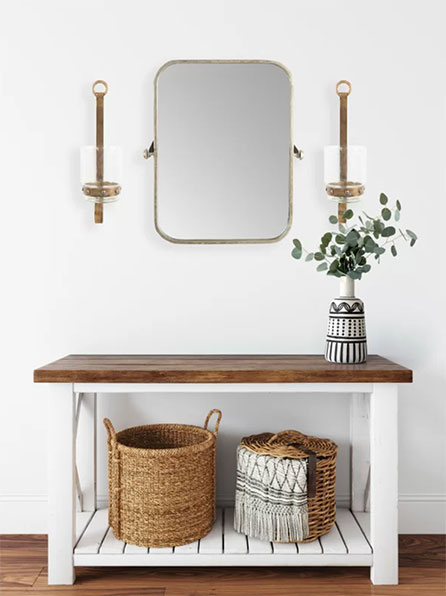 brass gold accent mirror hanging on white wall above wooden console table with baskets underneath