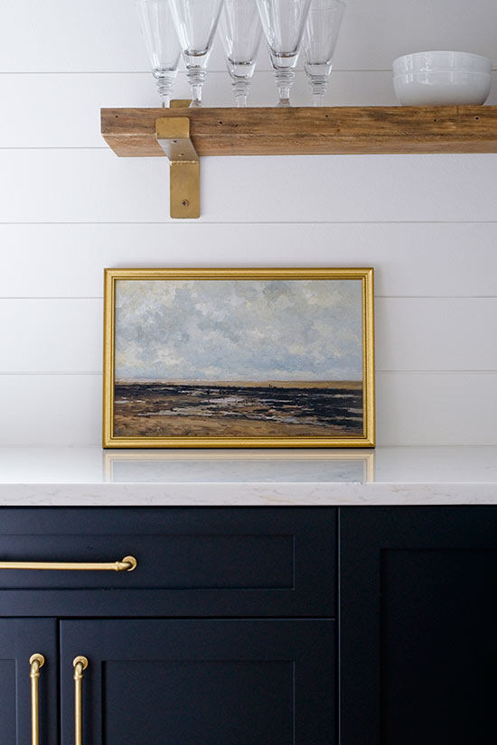 navy blue kitchen cabinets with vintage artwork leaning on counter with open shelving above
