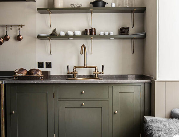 olive green English kitchen cabinets with vintage black and brass stove and open shelving and window seat