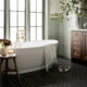 grey-green modern farmhouse bathroom with freestanding bathtub and black limestone herringbone tile floor and dark wood bath vanity