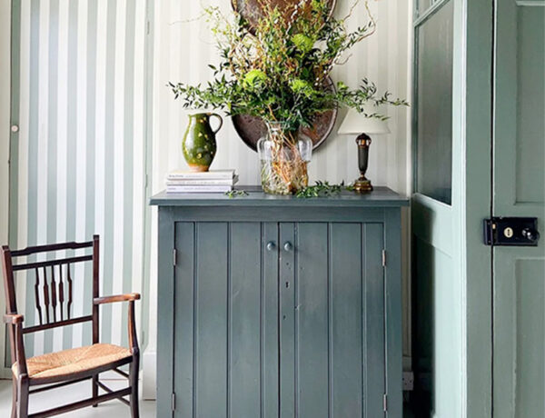 charming English cottage entryway foyer with primitive dark blue cabinet and vintage caning chair and striped wallpaper